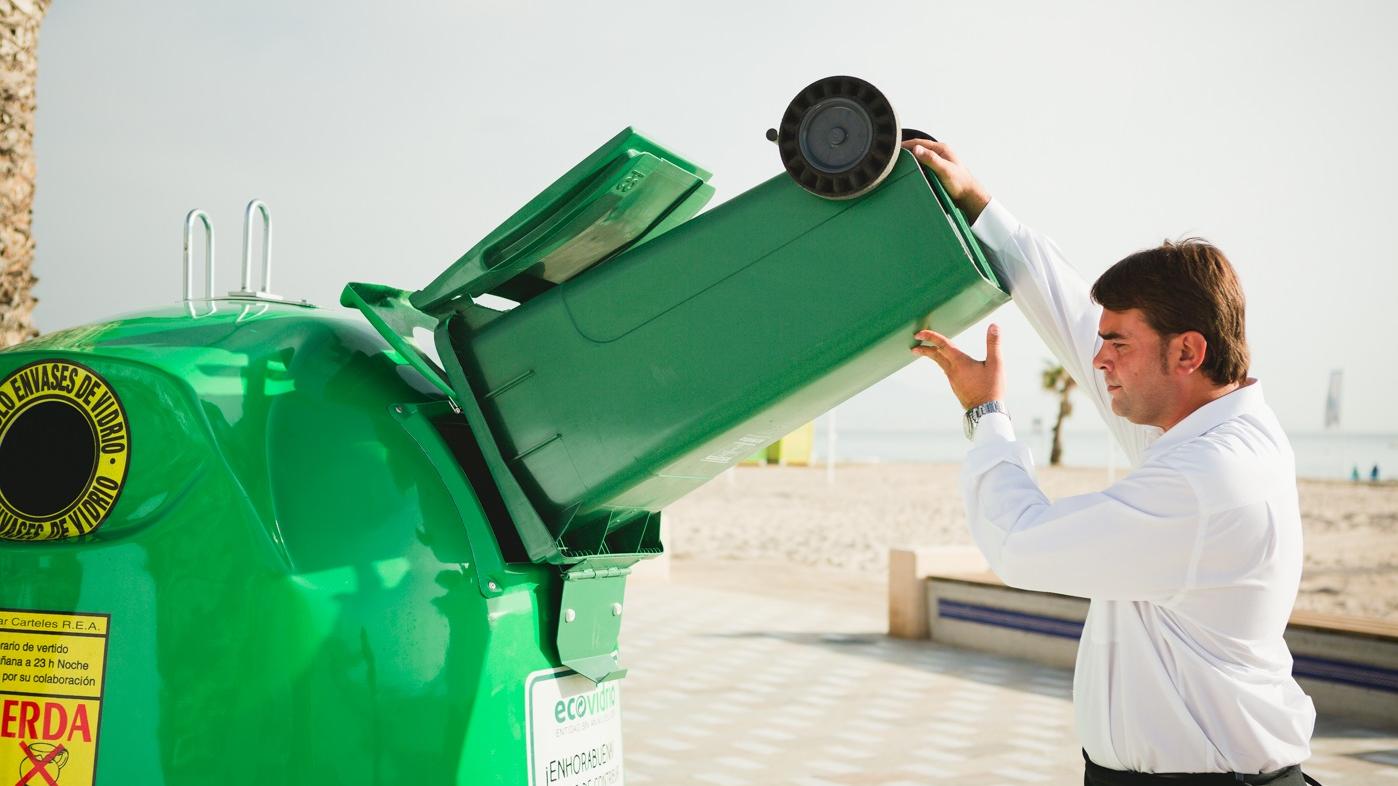 Camarero reciclando envases de vidrio con cubo
